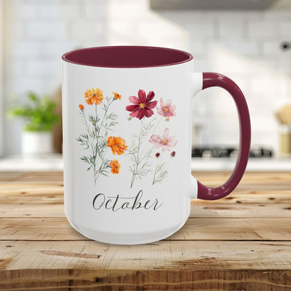White 15oz ceramic mug with maroon handle and interior, featuring watercolor cosmos and marigold flowers and "October" script.