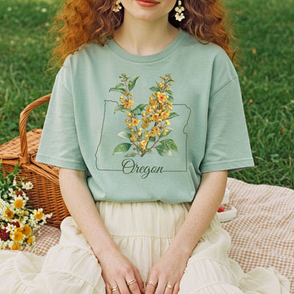 Garment-dyed sage green t-shirt with a hand-drawn Oregon outline and warm yellow Oregon Grape blossoms.
