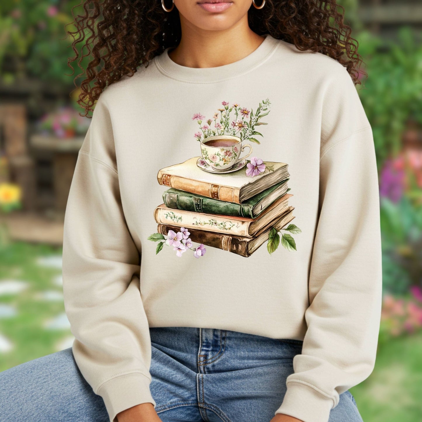 Beige crewneck sweatshirt with a vintage illustration of stacked books, a floral teacup, and greenery.