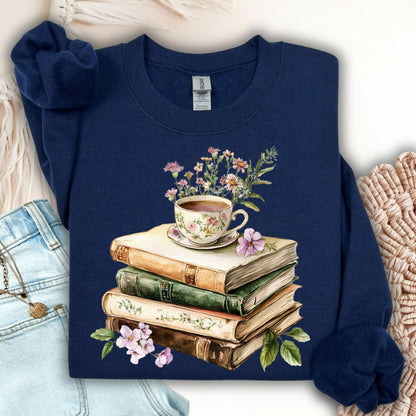 Dark navy crewneck sweatshirt with a vintage illustration of stacked books, a floral teacup, and greenery.