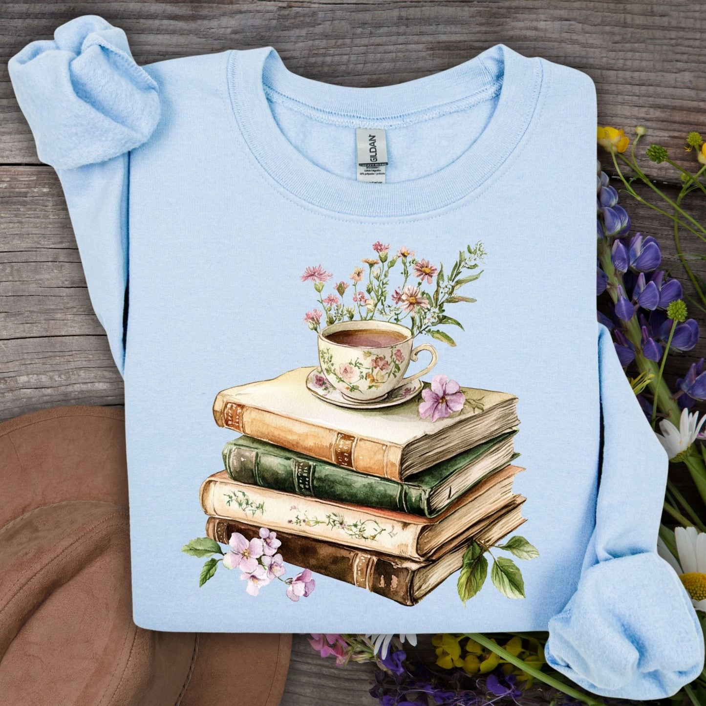 Light blue crewneck sweatshirt with a vintage illustration of stacked books, a floral teacup, and greenery.