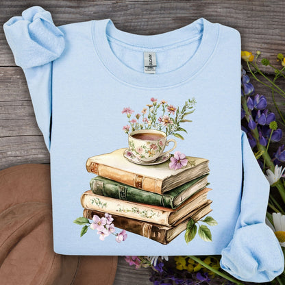 Light blue crewneck sweatshirt with a vintage illustration of stacked books, a floral teacup, and greenery.