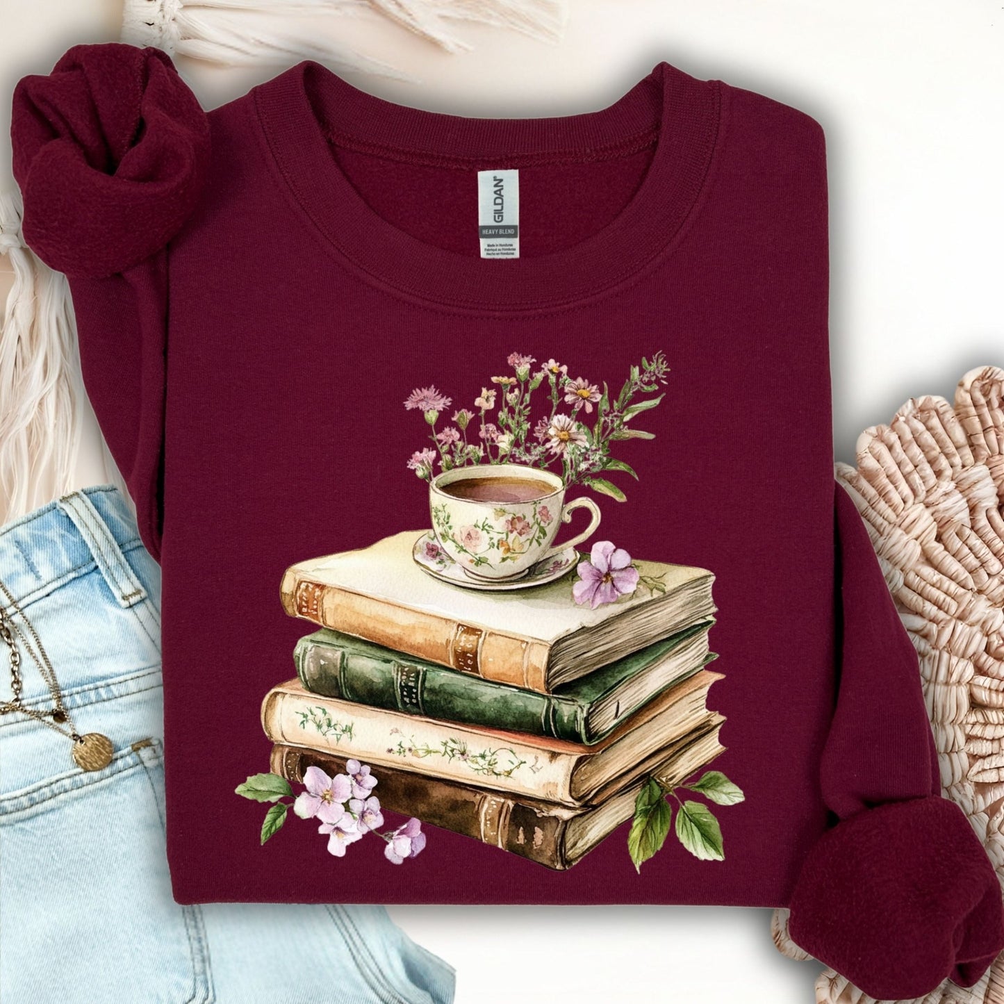 Maroon crewneck sweatshirt with a vintage illustration of stacked books, a floral teacup, and greenery.