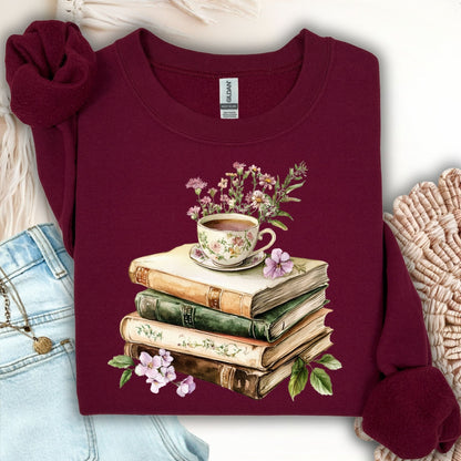 Maroon crewneck sweatshirt with a vintage illustration of stacked books, a floral teacup, and greenery.