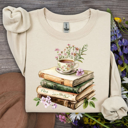 Sand crewneck sweatshirt with a vintage illustration of stacked books, a floral teacup, and greenery.