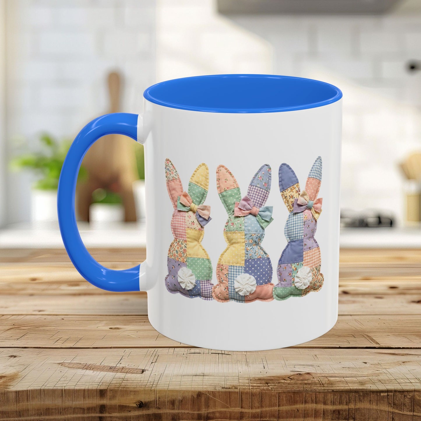 White ceramic mug with a blue handle and interior, featuring three pastel patchwork bunnies.