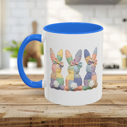 White ceramic mug with a blue handle and interior, featuring three pastel patchwork bunnies.