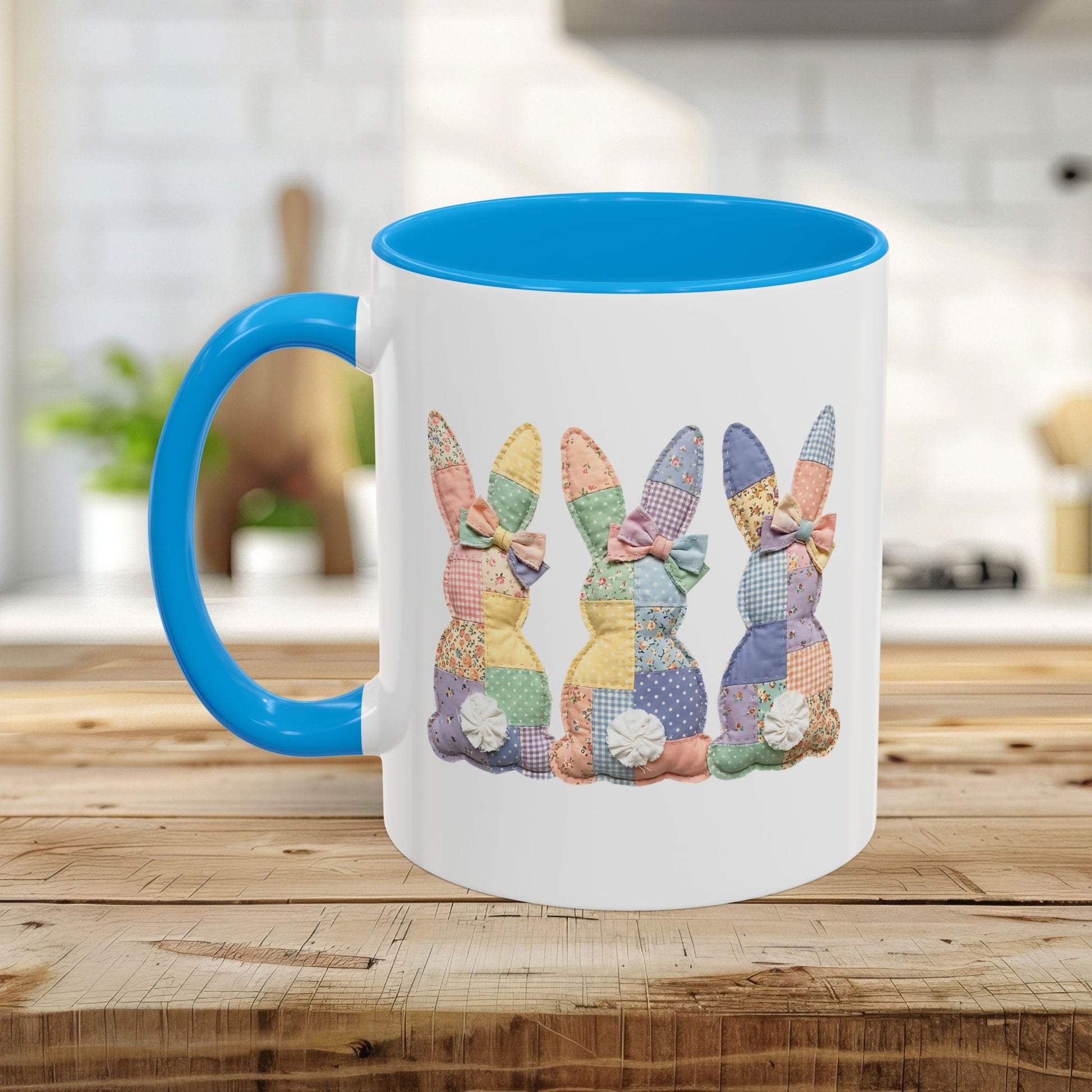 White ceramic mug with blue handle and interior, featuring three pastel patchwork bunnies.