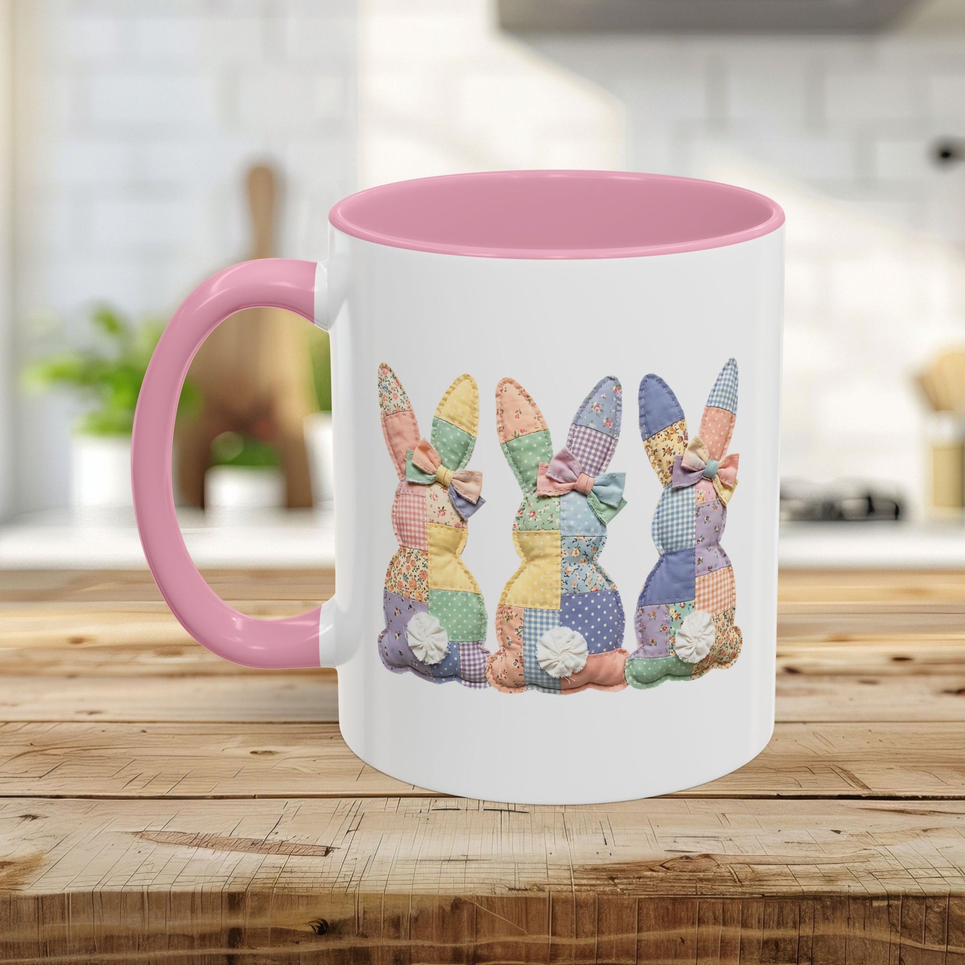 White ceramic mug with pink handle and interior, featuring three pastel patchwork bunnies.