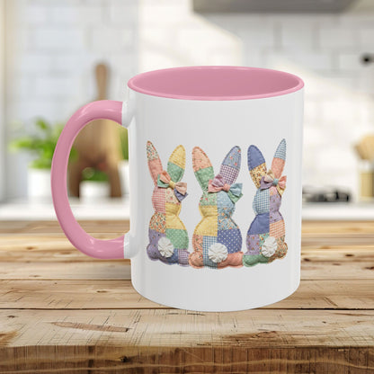 White ceramic mug with pink handle and interior, featuring three pastel patchwork bunnies.