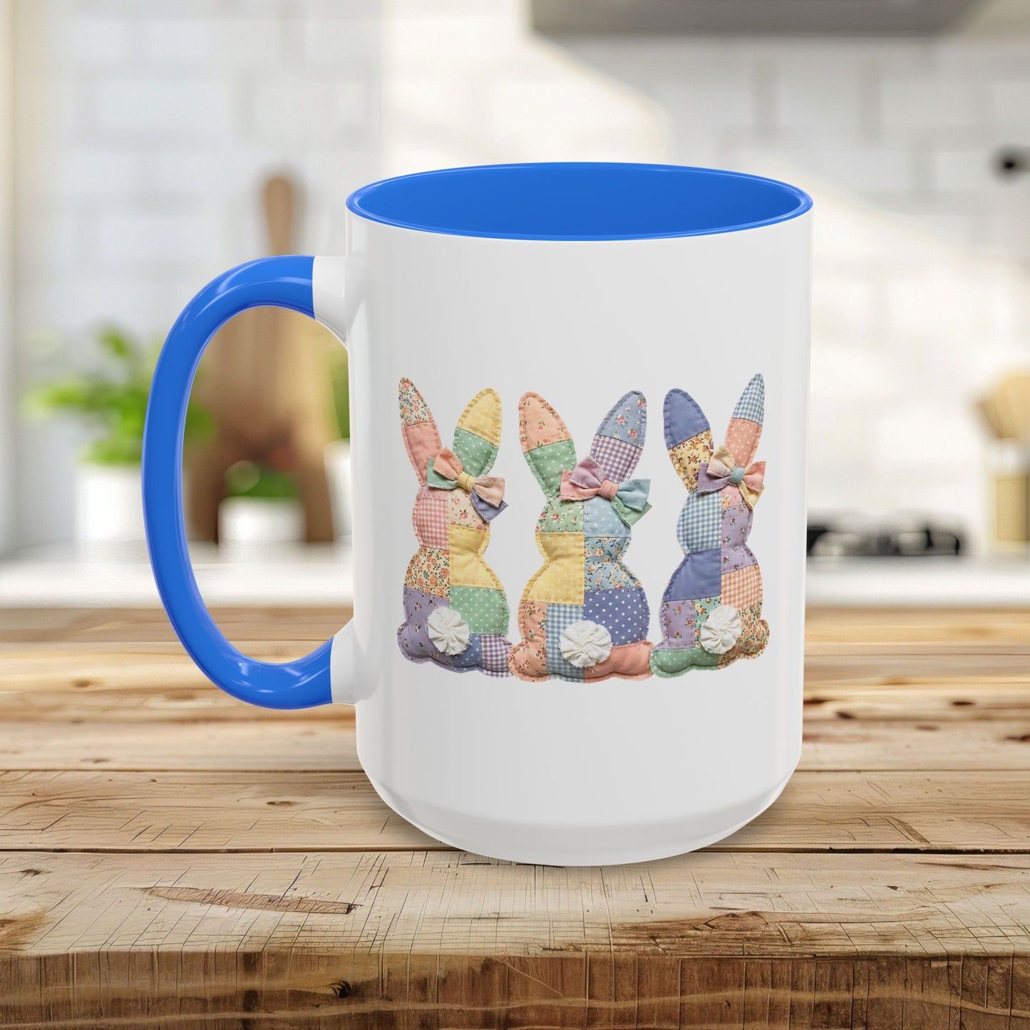 White ceramic mug with blue handle and interior, featuring three pastel patchwork bunnies.