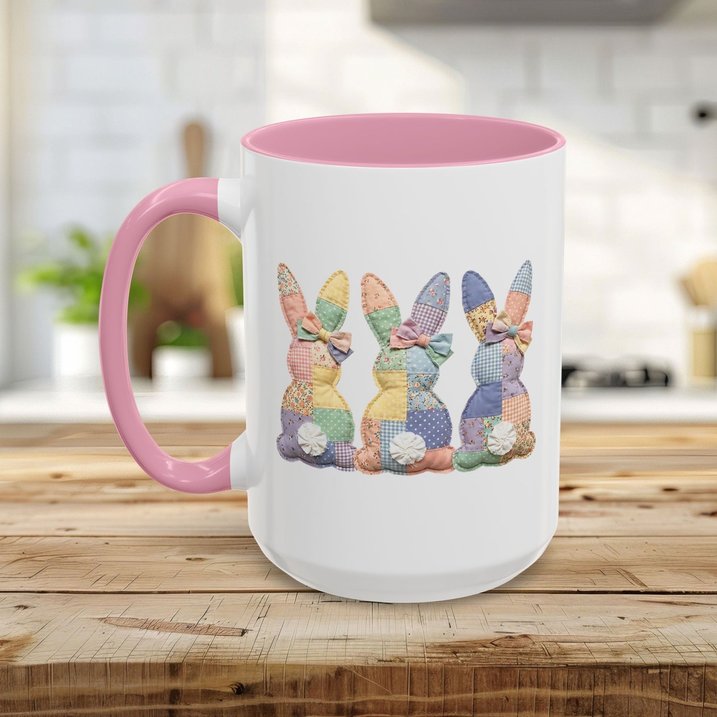 White ceramic mug with pink handle and interior, featuring three pastel patchwork bunnies.