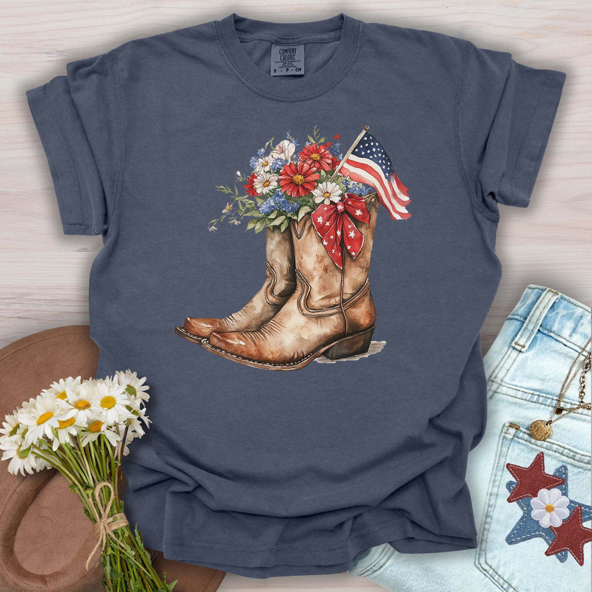 Navy t-shirt with watercolor cowboy boots, red, white, and blue flowers, and an American flag.
