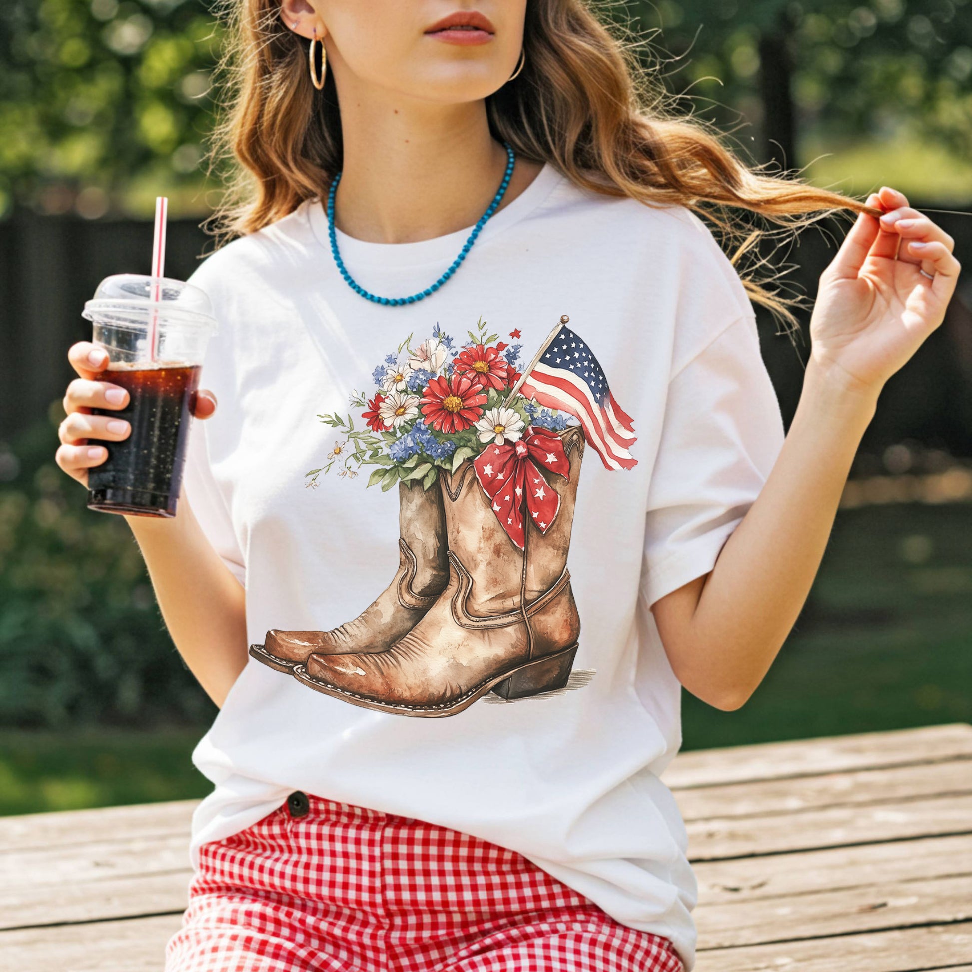 White t-shirt with watercolor cowboy boots, vibrant flowers, an American flag, and star ribbon.