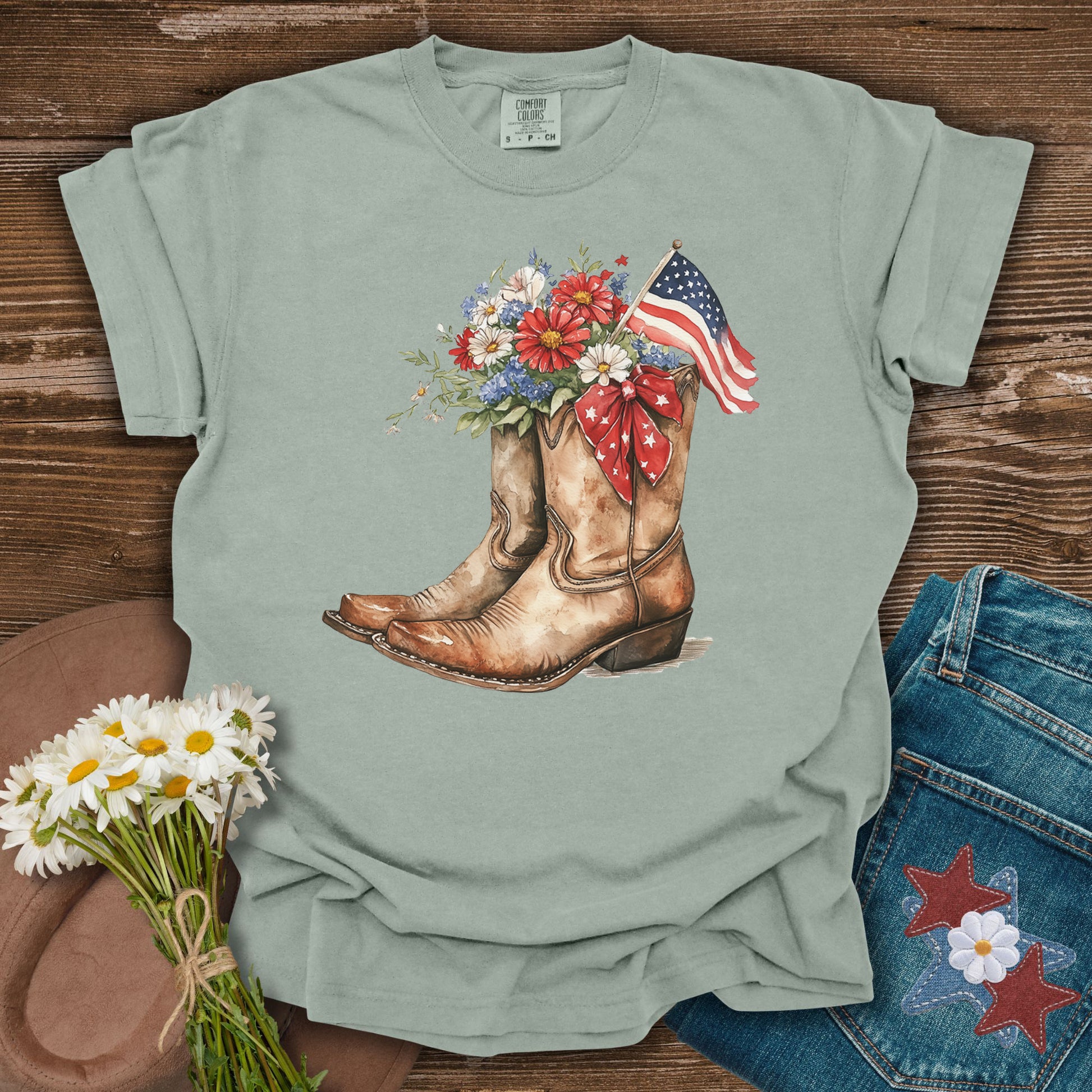 Bay S t-shirt with watercolor cowboy boots, flowers, and an American flag.