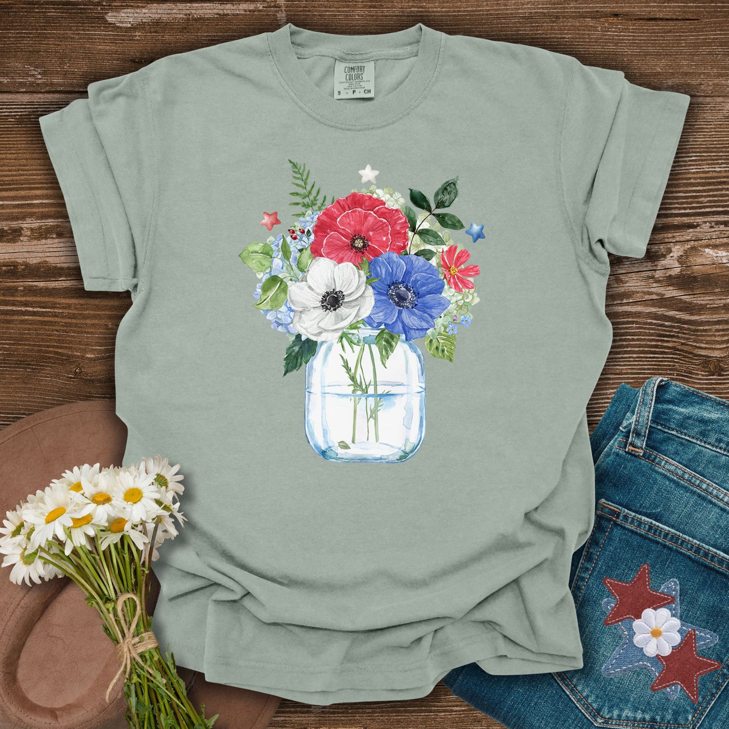 Bay S t-shirt with a watercolor patriotic floral bouquet in a mason jar, featuring red, white, and blue anemones and stars.