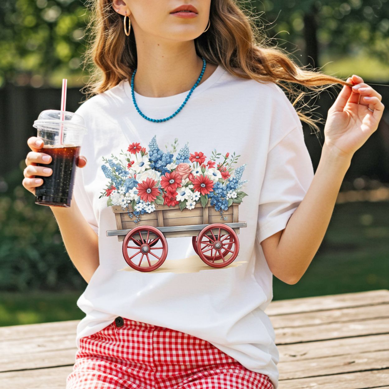 White garment-dyed cotton t-shirt with a hand-painted wagon overflowing with red, white, and blue florals.