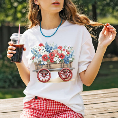 White garment-dyed cotton t-shirt with a hand-painted wagon overflowing with red, white, and blue florals.