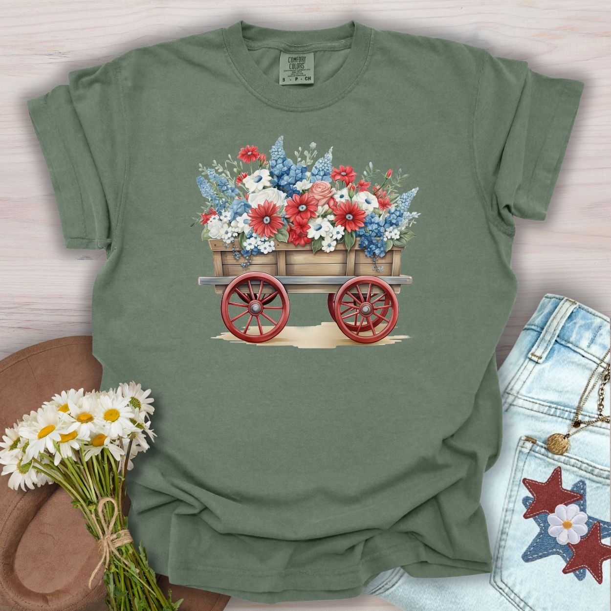 Moss green garment-dyed cotton t-shirt with a patriotic flower wagon design, surrounded by daisies and jeans.