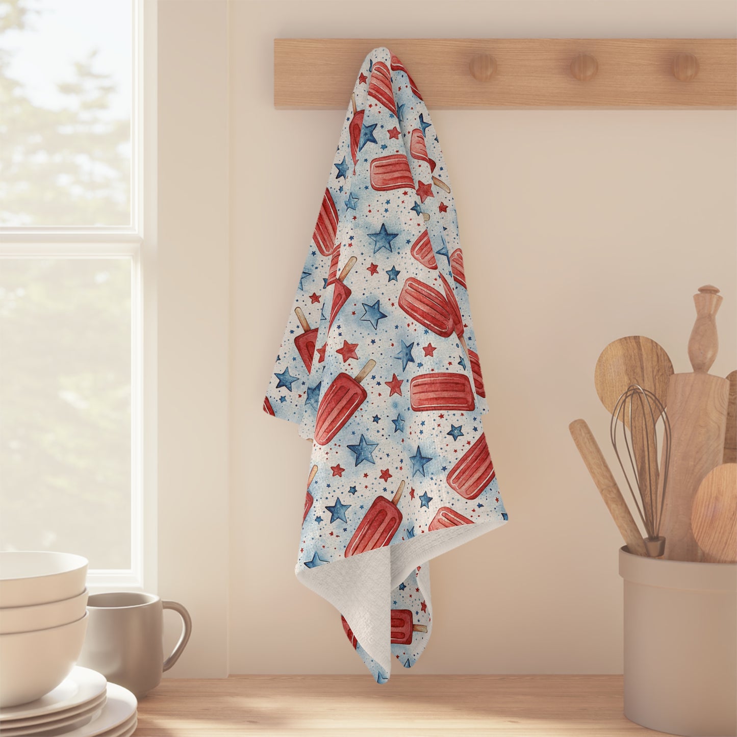 Patriotic microfiber tea towel with red popsicles and blue stars, hanging on a wooden peg.