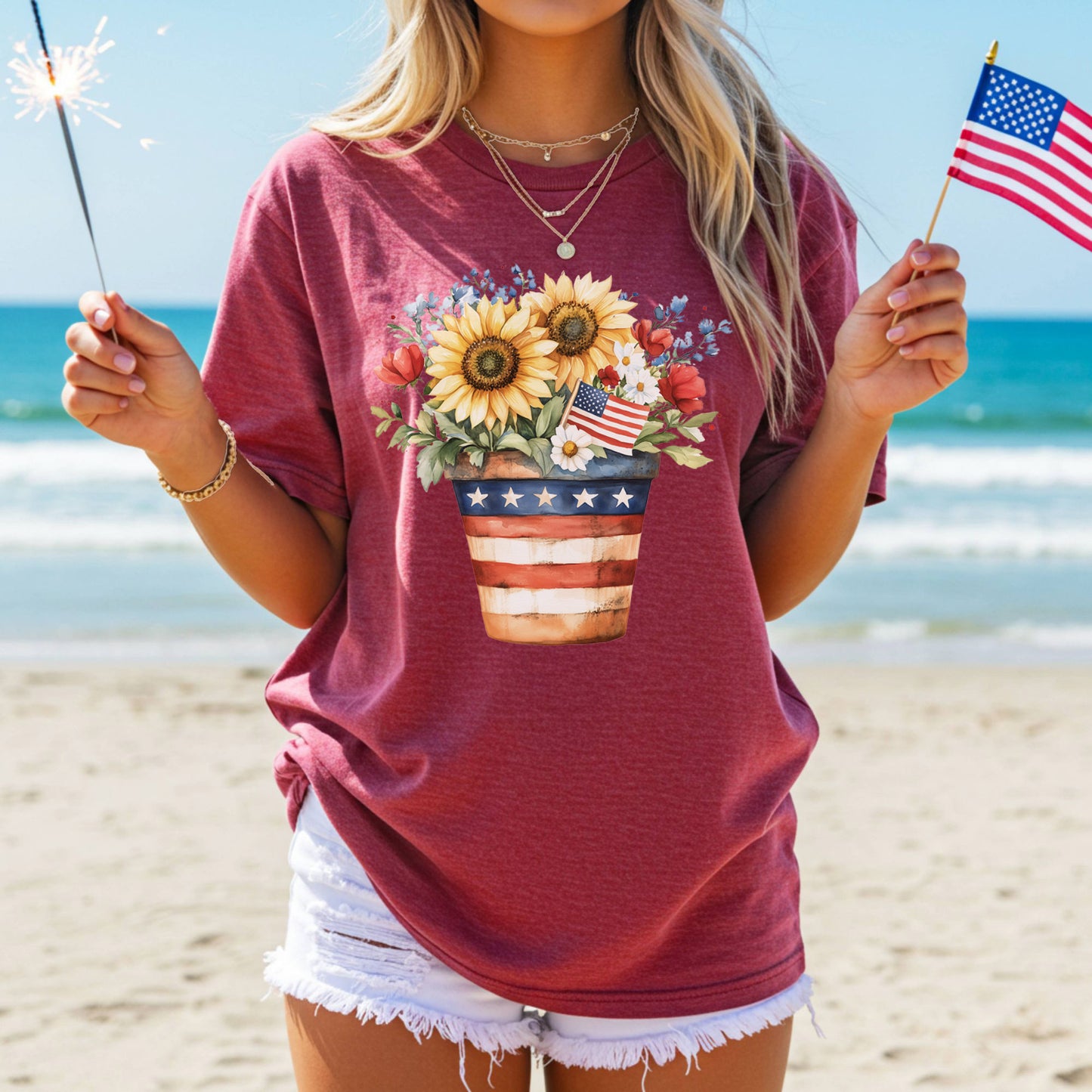 Woman in a red t-shirt with a patriotic sunflower bouquet design, holding a sparkler and American flag.