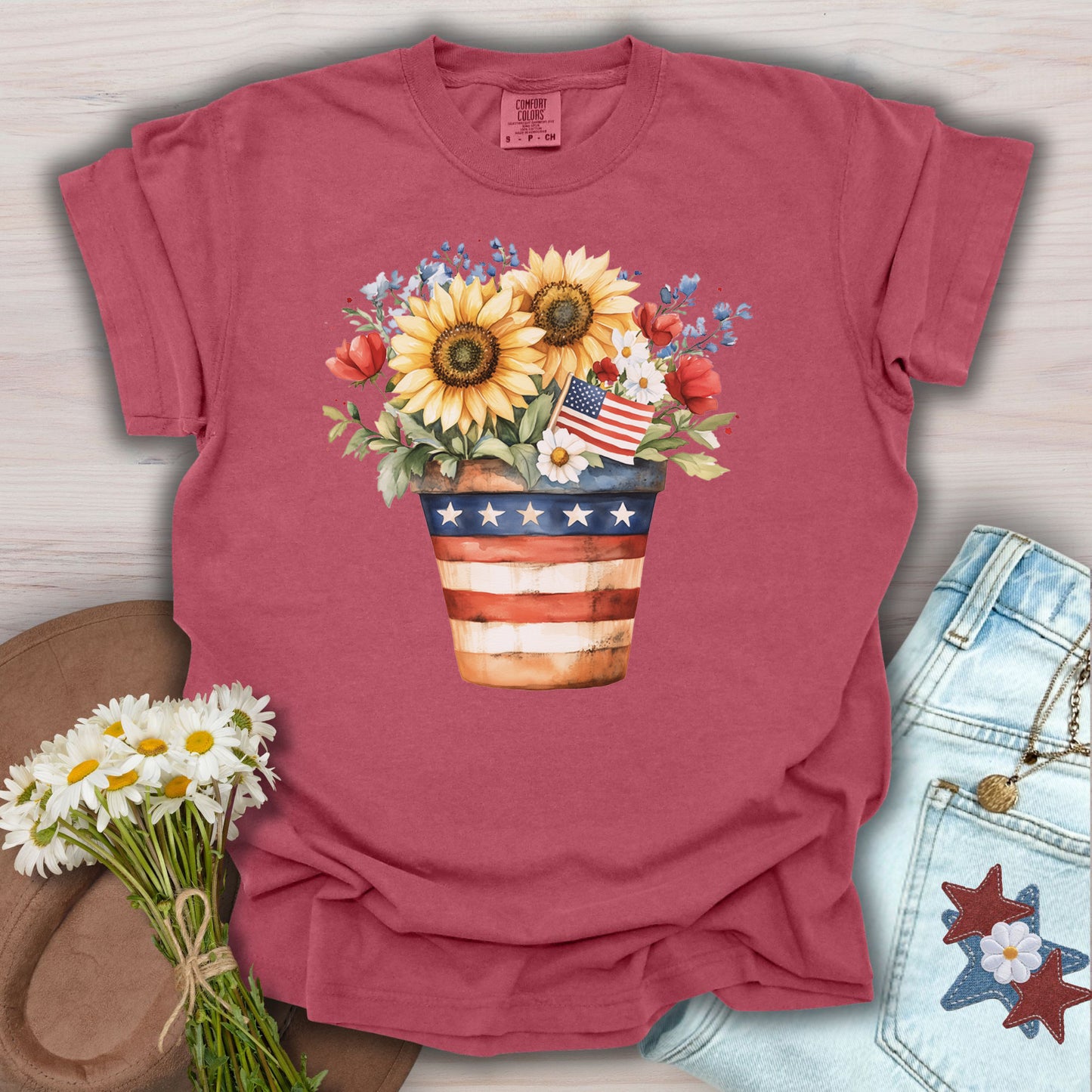 Crimson S t-shirt with a patriotic sunflower bouquet in an American flag pot, featuring daisies, roses, and blue forget-me-nots.