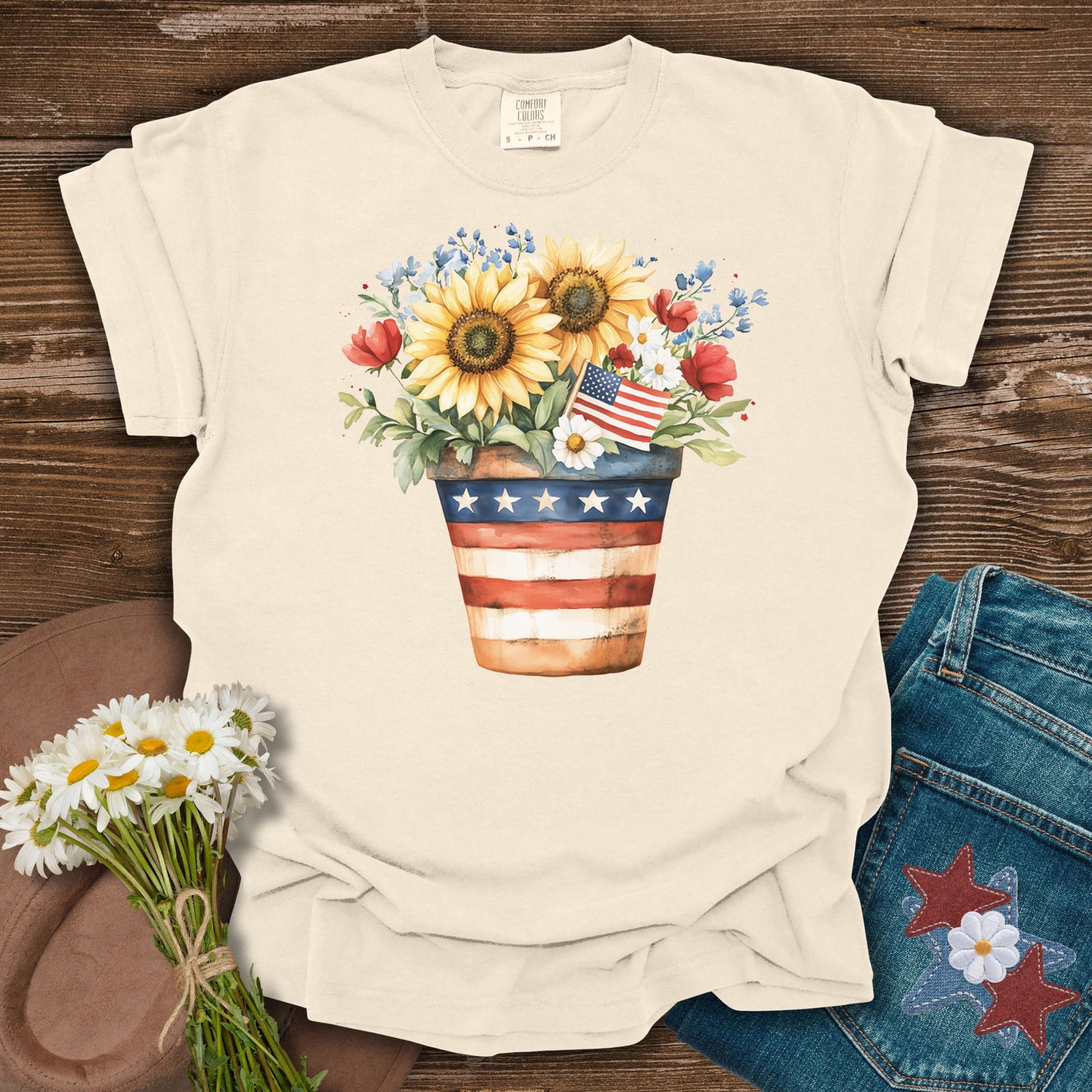 Ivory S t-shirt with a patriotic sunflower, daisy, rose, and forget-me-not bouquet in an American flag pot.