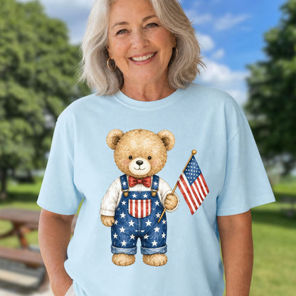 Woman in a light blue t-shirt featuring a hand-drawn teddy bear in Americana overalls holding an American flag.