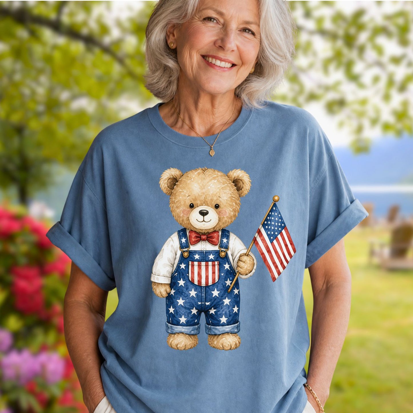 Woman in a blue garment-dyed t-shirt with a hand-drawn teddy bear in Americana overalls holding a flag.