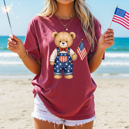Garment-dyed red t-shirt with a hand-drawn teddy bear in Americana overalls holding a flag.