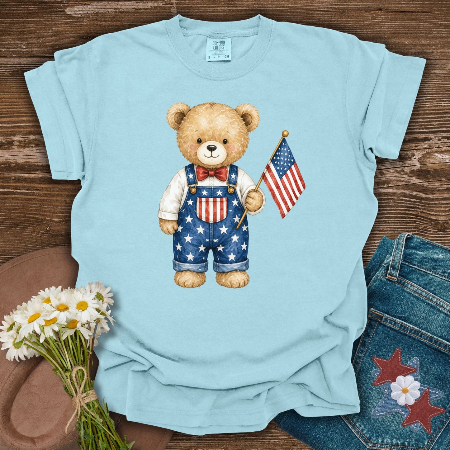 Chambray blue t-shirt with a hand-drawn teddy bear in Americana overalls holding a US flag.