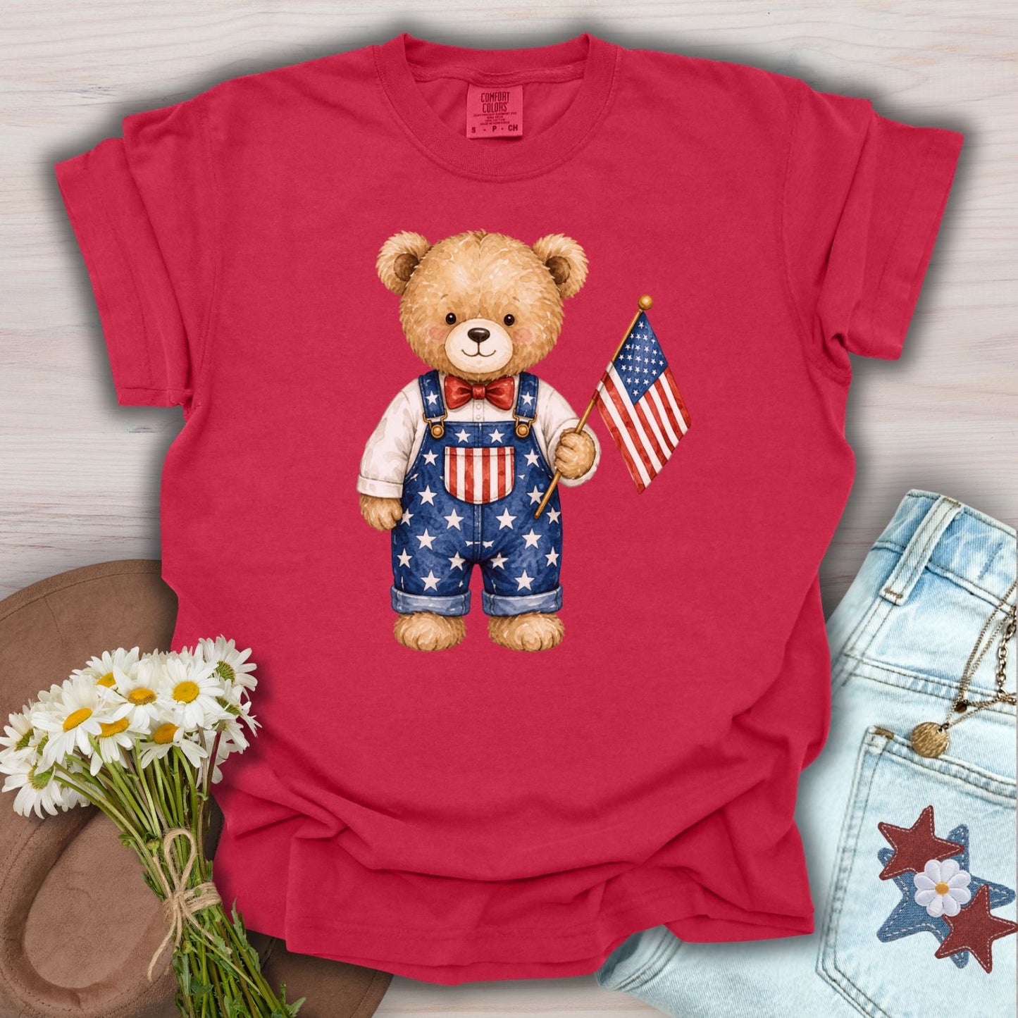 Red S-size garment-dyed cotton t-shirt with a hand-drawn teddy bear in Americana overalls holding a flag.