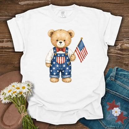 White S t-shirt with a hand-drawn teddy bear in Americana overalls holding a US flag.