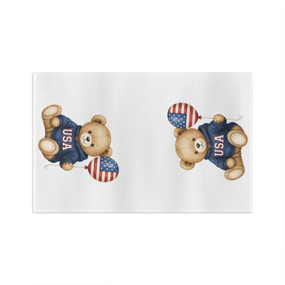 White microfiber tea towel with two watercolor-style teddy bears in USA sweatshirts holding flag balloons.