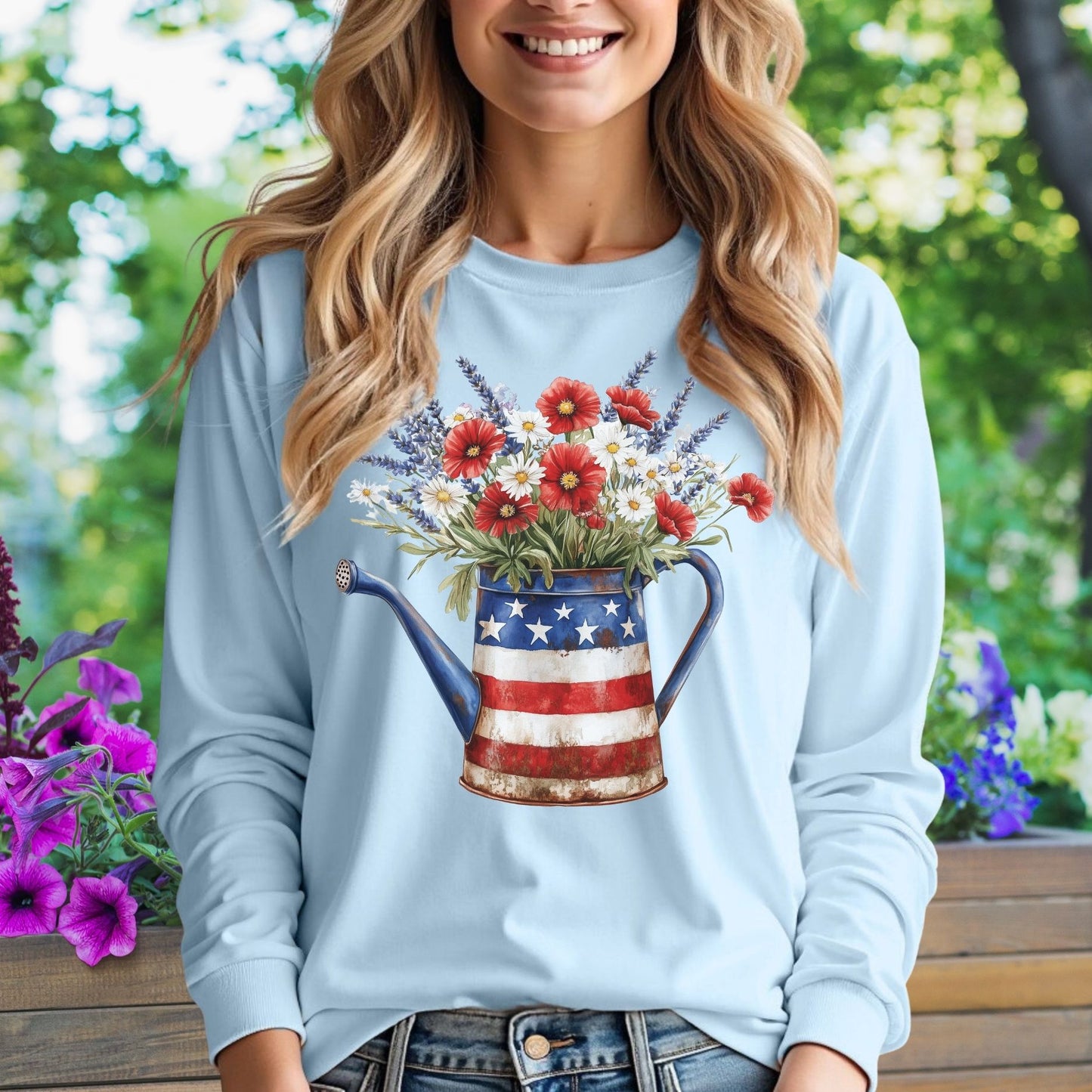 Light blue long sleeve tee with a rustic patriotic watering can holding red, white, and blue wildflowers.