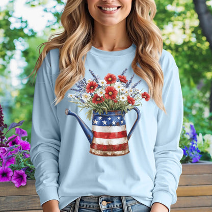 Light blue long sleeve tee with a rustic patriotic watering can holding red, white, and blue wildflowers.