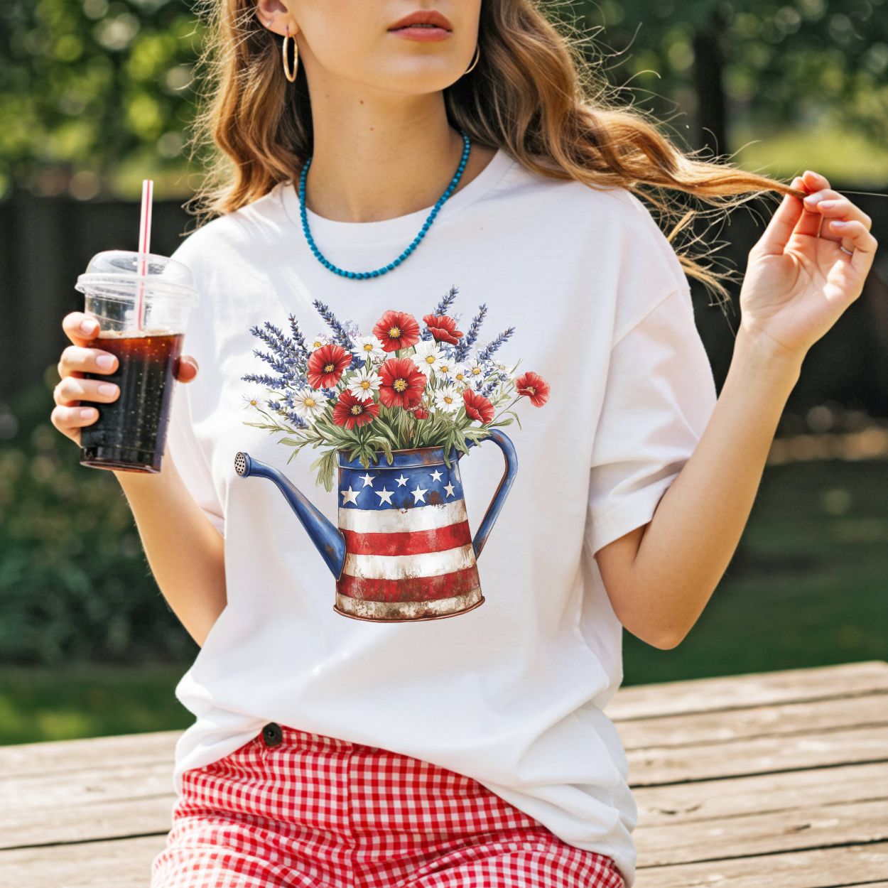White t-shirt with a rustic patriotic watering can overflowing with red poppies, daisies, and lavender.