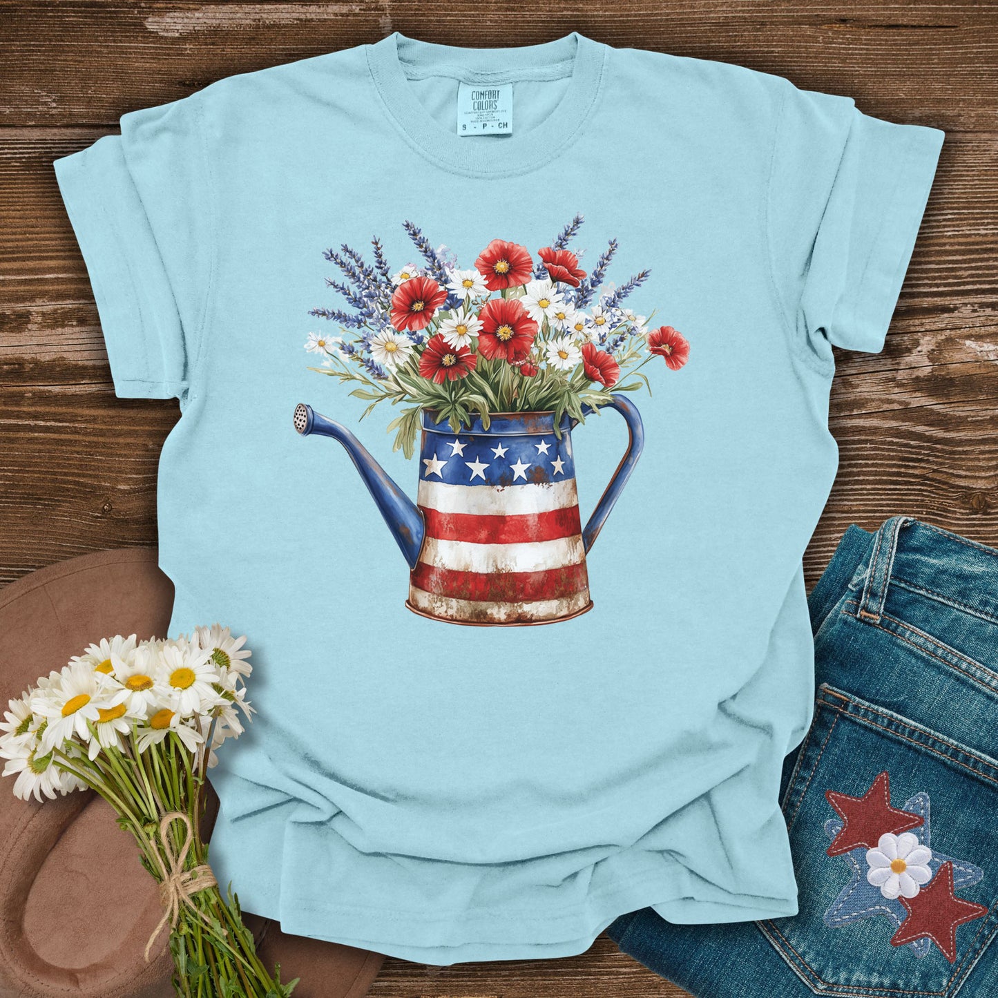 Chambray blue t-shirt with a rustic patriotic watering can overflowing with lavender, daisies, and red poppies.