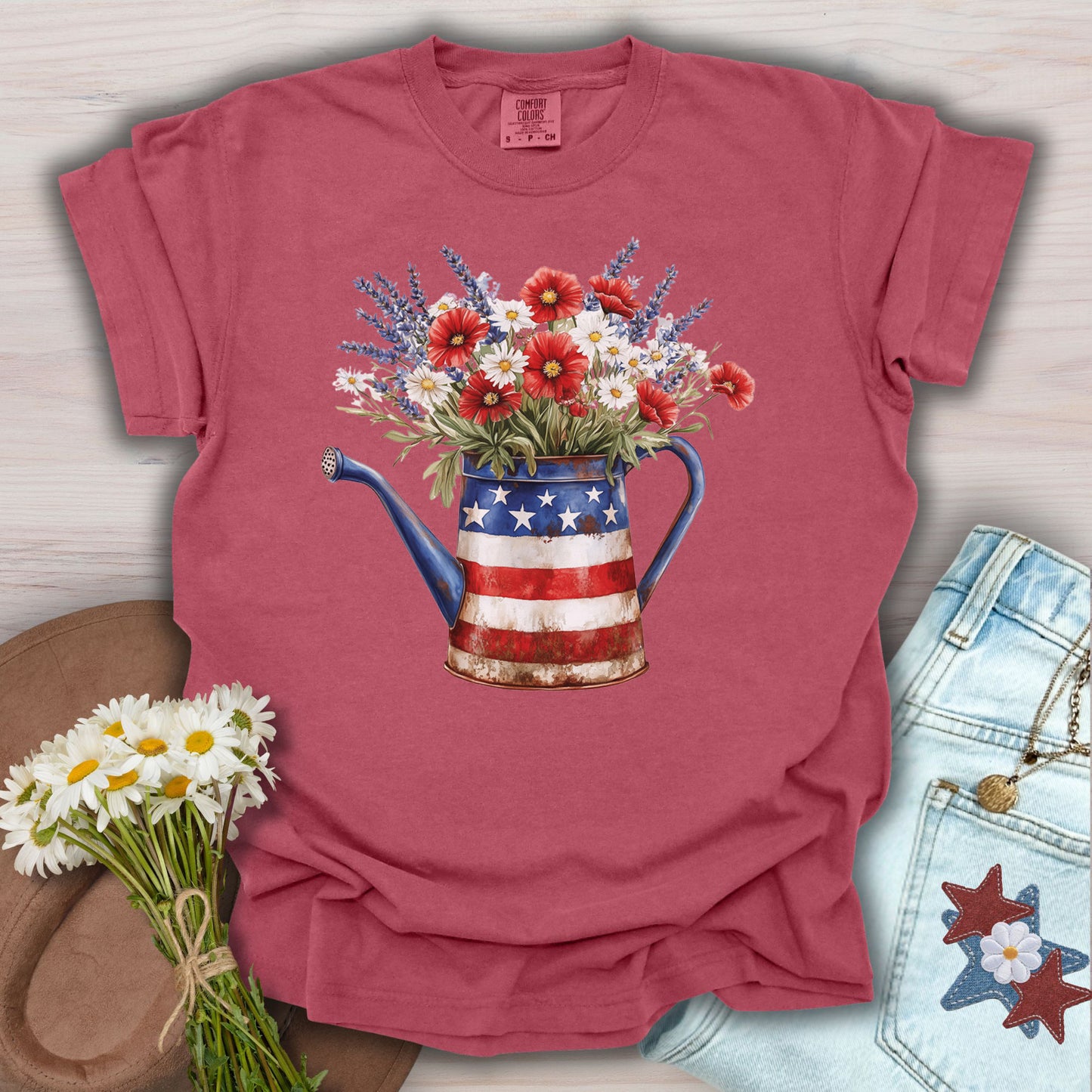 Crimson S t-shirt with a rustic patriotic watering can overflowing with lavender, daisies, and red poppies.