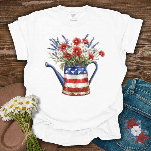 White S t-shirt with a rustic patriotic watering can overflowing with lavender, daisies, and red poppies.