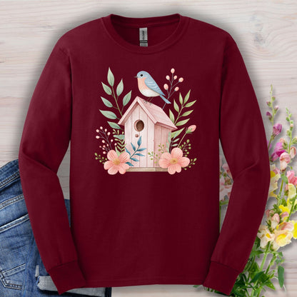 Maroon long sleeve tee with a pink birdhouse, blue bird, and botanical watercolor illustration.