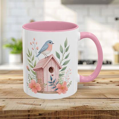 White ceramic mug with pink interior and handle, featuring a bluebird on a pink birdhouse with peach blossoms.