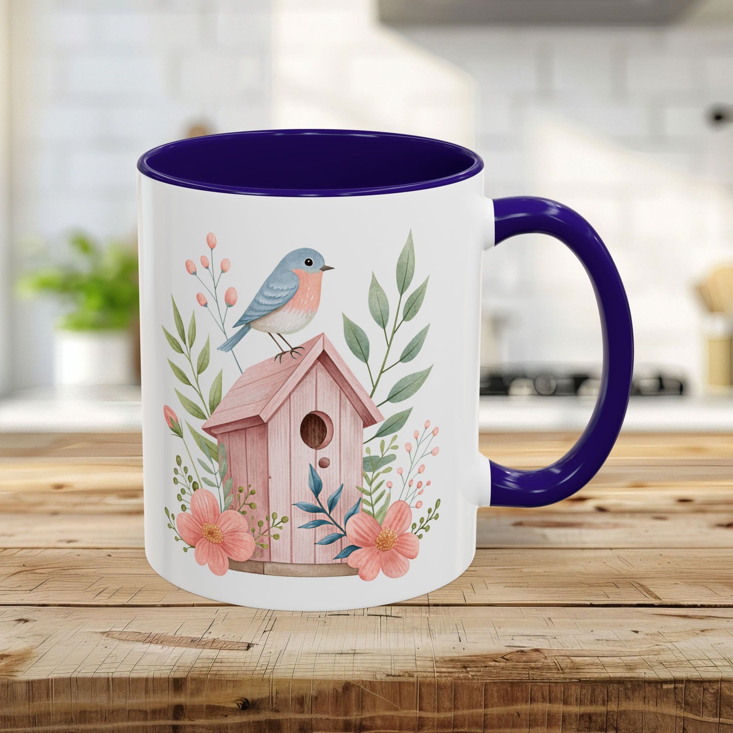 White 11oz ceramic mug with blue interior/handle, featuring a watercolor pink birdhouse, bluebird, and peach blossoms.