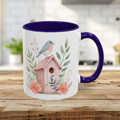 White 11oz ceramic mug with blue interior/handle, featuring a watercolor pink birdhouse, bluebird, and peach blossoms.