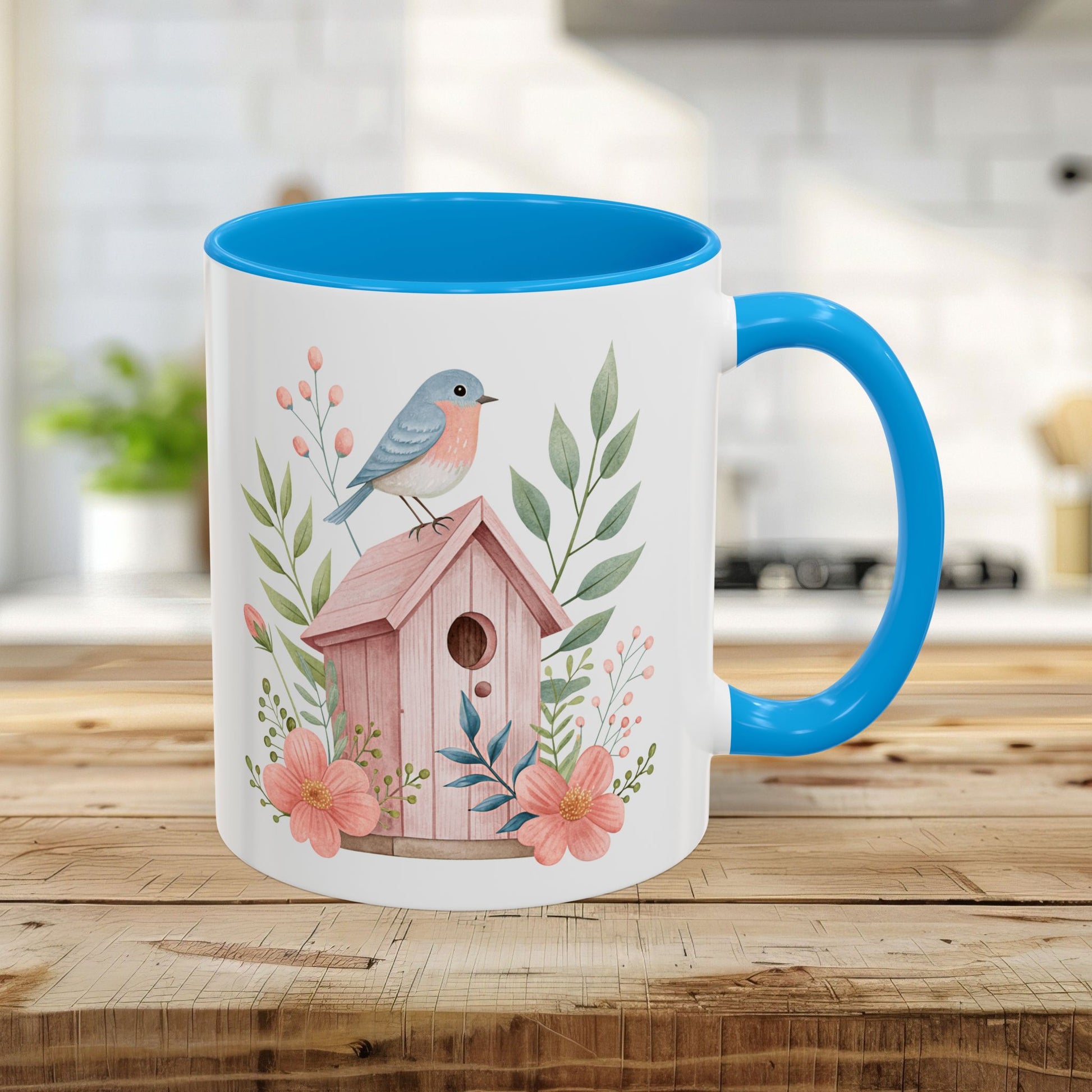White ceramic 11oz mug with light blue interior/handle, featuring a watercolor pink birdhouse, bluebird, and peach blossoms.