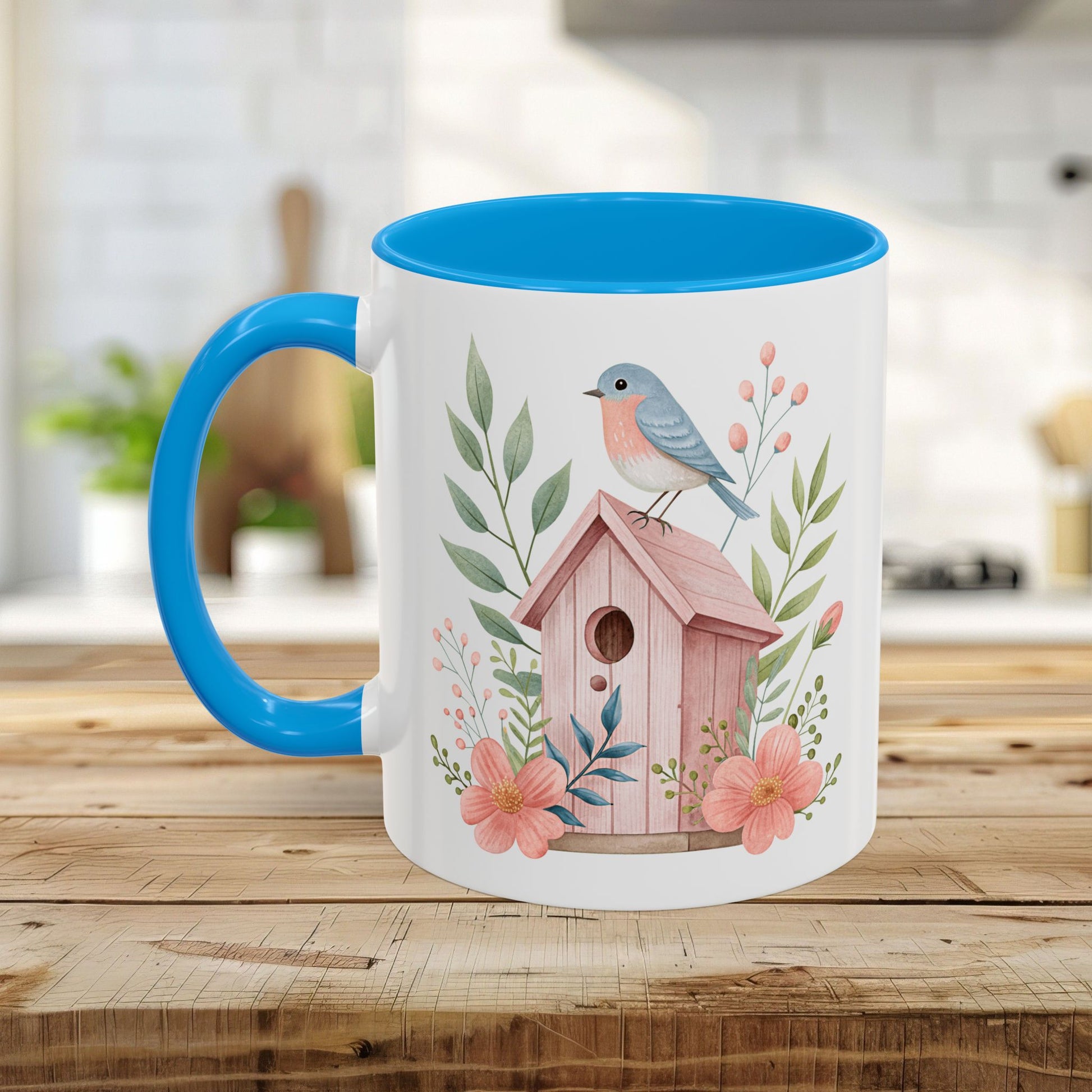 White ceramic mug with blue interior/handle, featuring a watercolor pink birdhouse, bluebird, and peach blossoms.