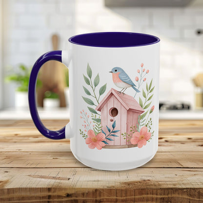 White ceramic mug with purple handle/interior, featuring a pink birdhouse, bluebird, and peach blossoms.