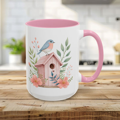 15oz white ceramic mug with pink interior/handle, featuring a watercolor birdhouse, bluebird, and peach blossoms.