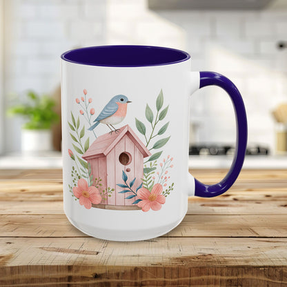 15oz white ceramic mug with blue interior/handle, featuring a watercolor pink birdhouse, bluebird, and peach blossoms.
