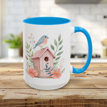 15oz white ceramic mug with light blue interior/handle, featuring a pink birdhouse, bluebird, and peach blossoms.